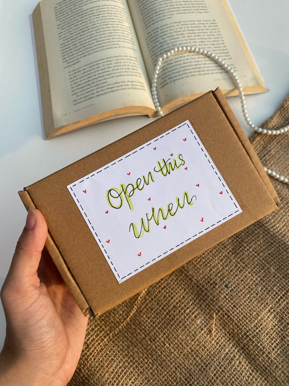 A hand holding a brown box labeled Open this when near an open book.