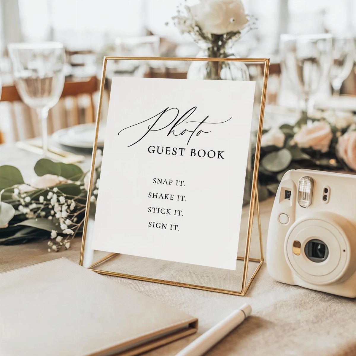 A photo guest book sign in a gold frame next to an instant camera and flowers.
