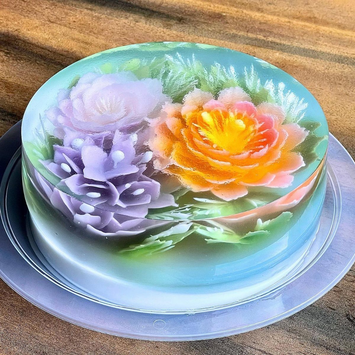 A translucent jelly cake featuring suspended purple and orange flowers with green leaves.