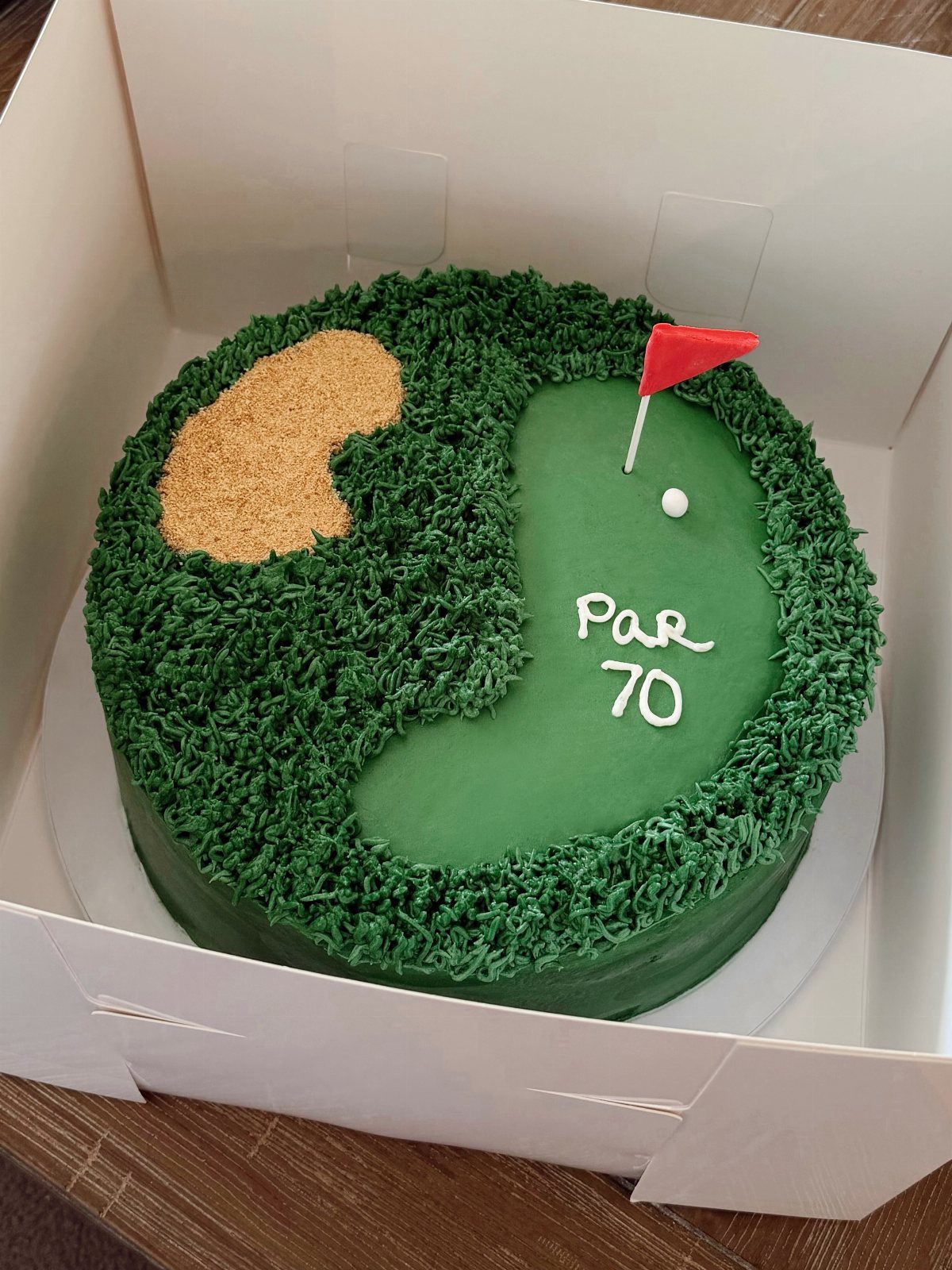 A golf course themed cake with a green grass texture, sand trap, and red flag.