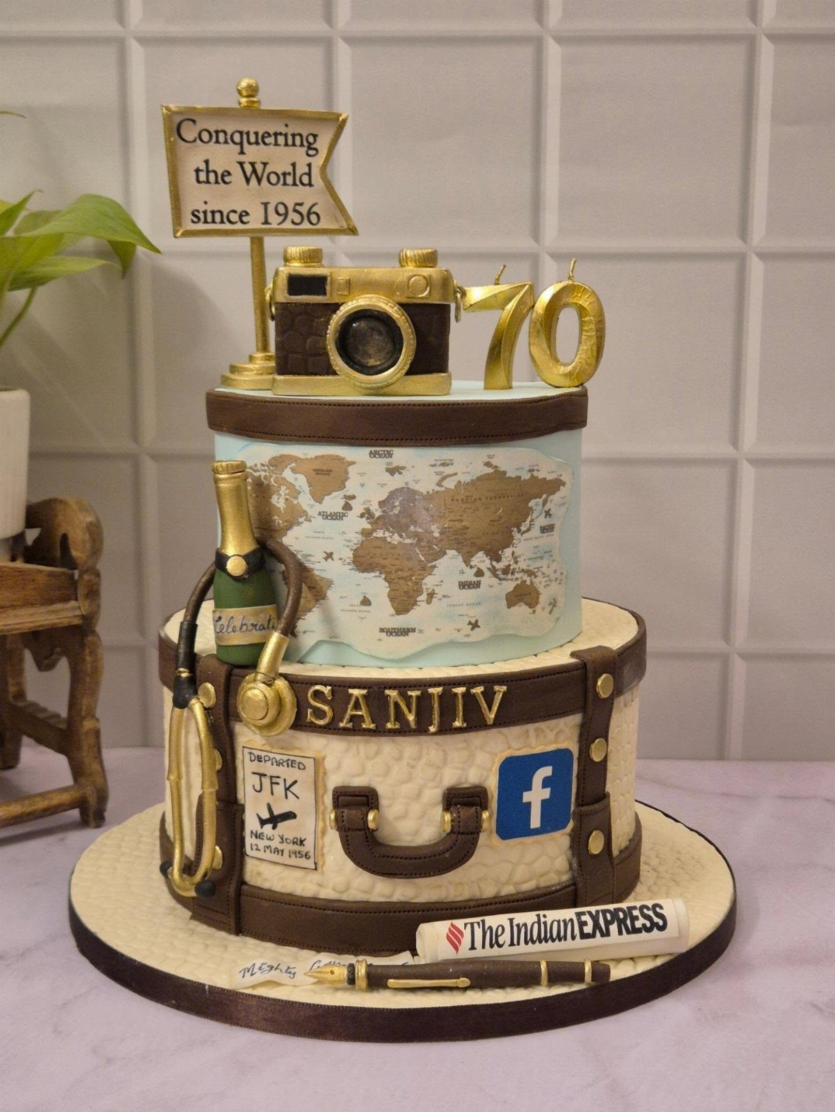 Two-tier travel themed cake featuring a world map, camera, and suitcase design with stickers.