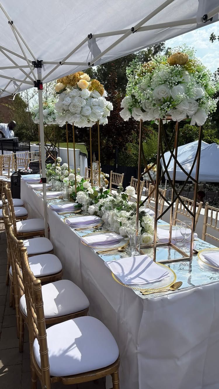 A long banquet table decorated with white flowers, gold accents, and elegant place settings under a canopy.