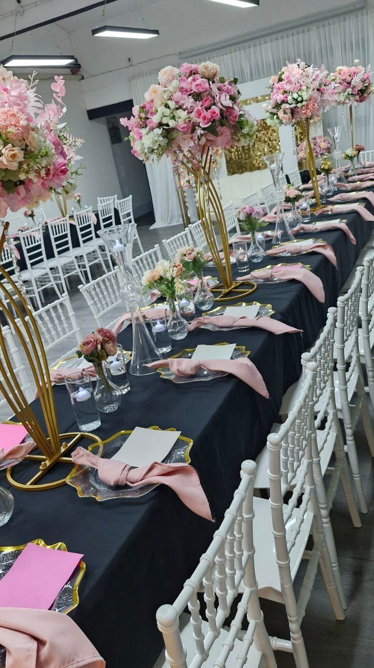 A long banquet table decorated with pink flowers, gold stands, and black linens for a celebration.
