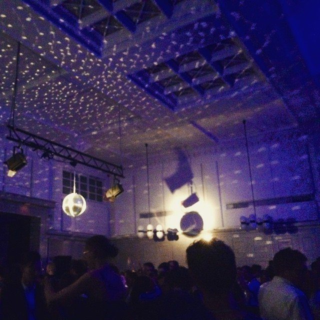 Silhouettes of people dancing under blue disco lights and a hanging disco ball in a dark room.