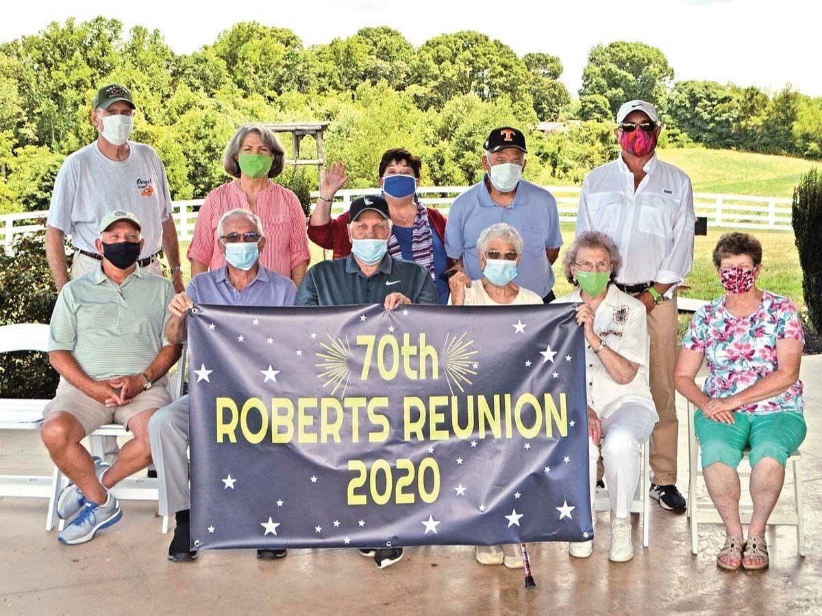 Group of masked adults posing outdoors holding a navy banner celebrating the 70th Roberts Reunion 2020.
