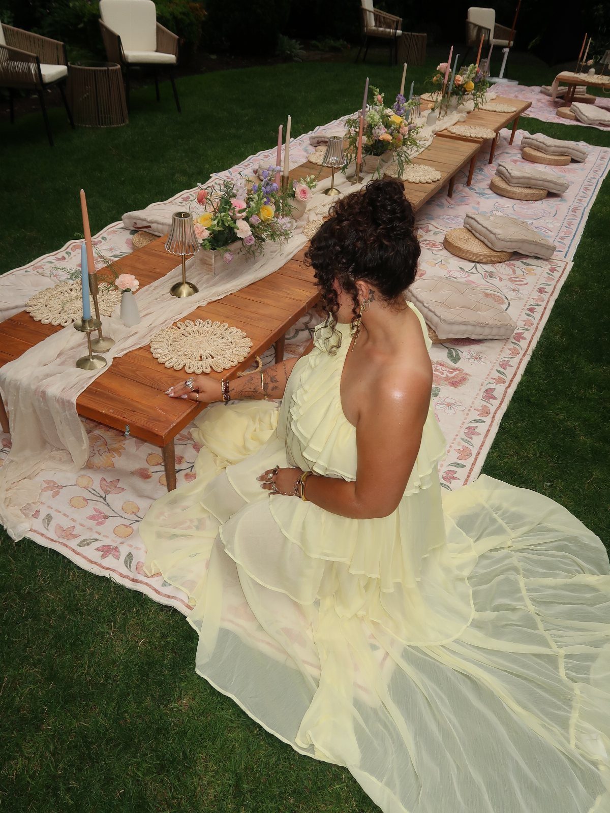 A woman in a yellow dress sits at a decorated outdoor garden party table.