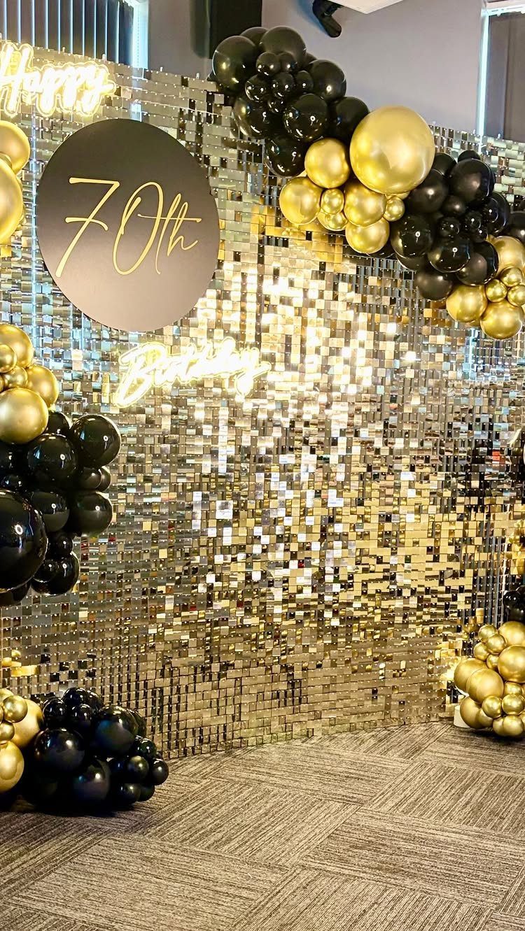 Gold sequin backdrop with black and gold balloon garlands and a 70th birthday sign.