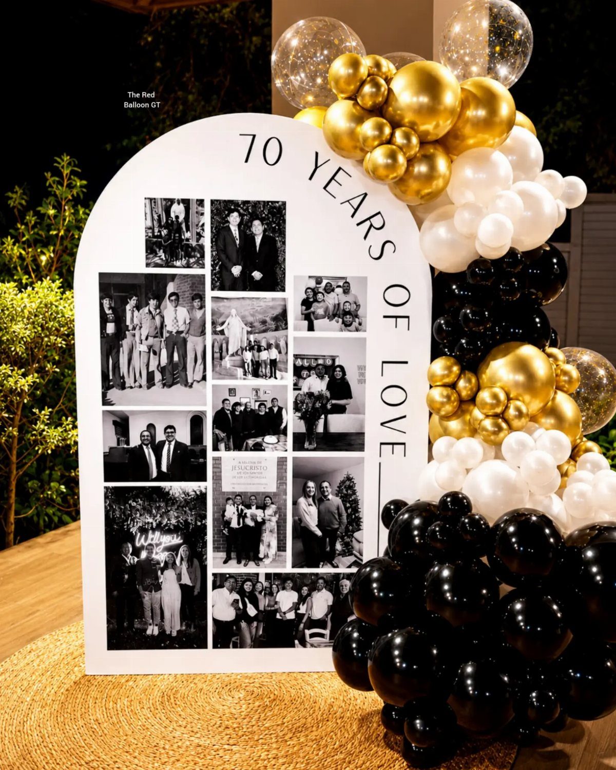 A white arched photo display sign decorated with gold, white, and black balloons.