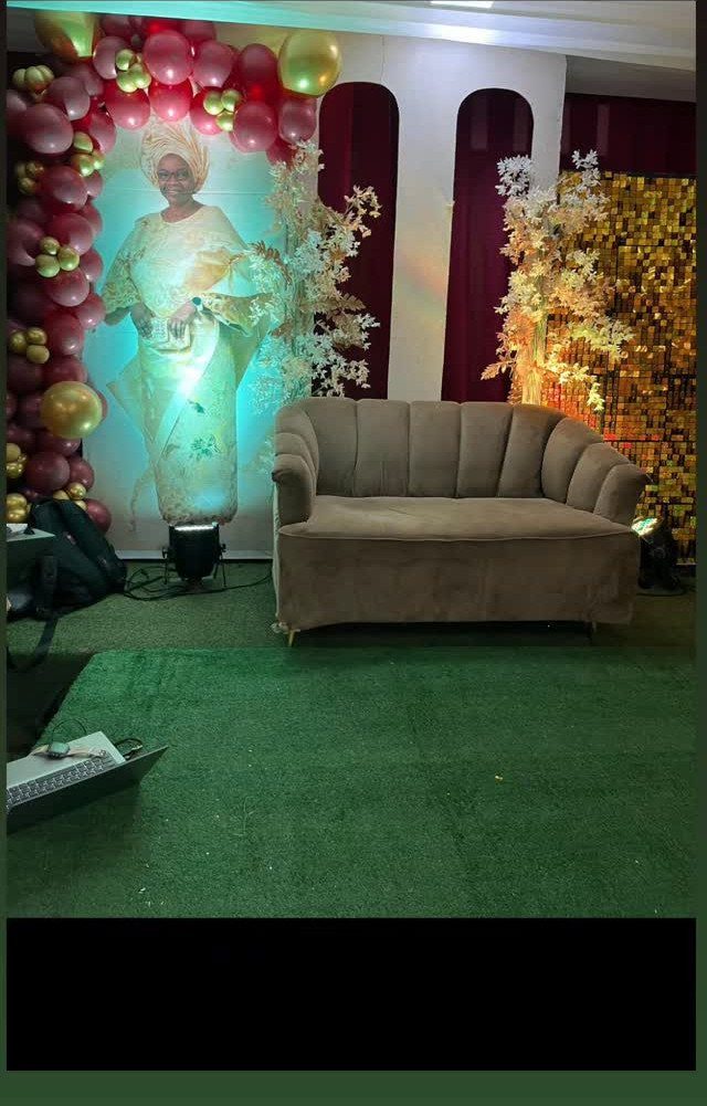 A celebratory event setup with balloon arches, a large portrait, and a velvet sofa.
