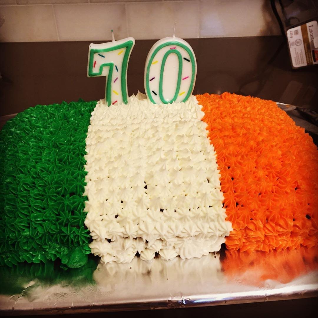 Rectangular cake with green white and orange frosting stripes and 70 candles on silver tray