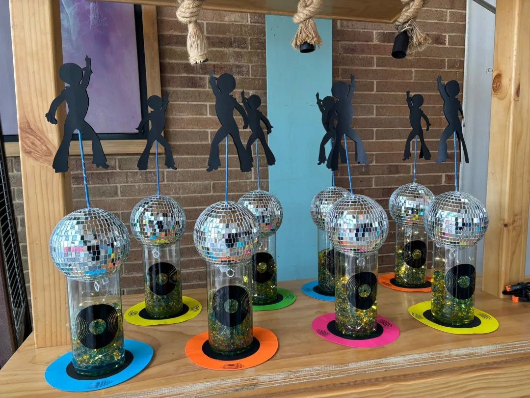 Disco ball centerpieces with dancing silhouettes and vinyl records on a wooden table.