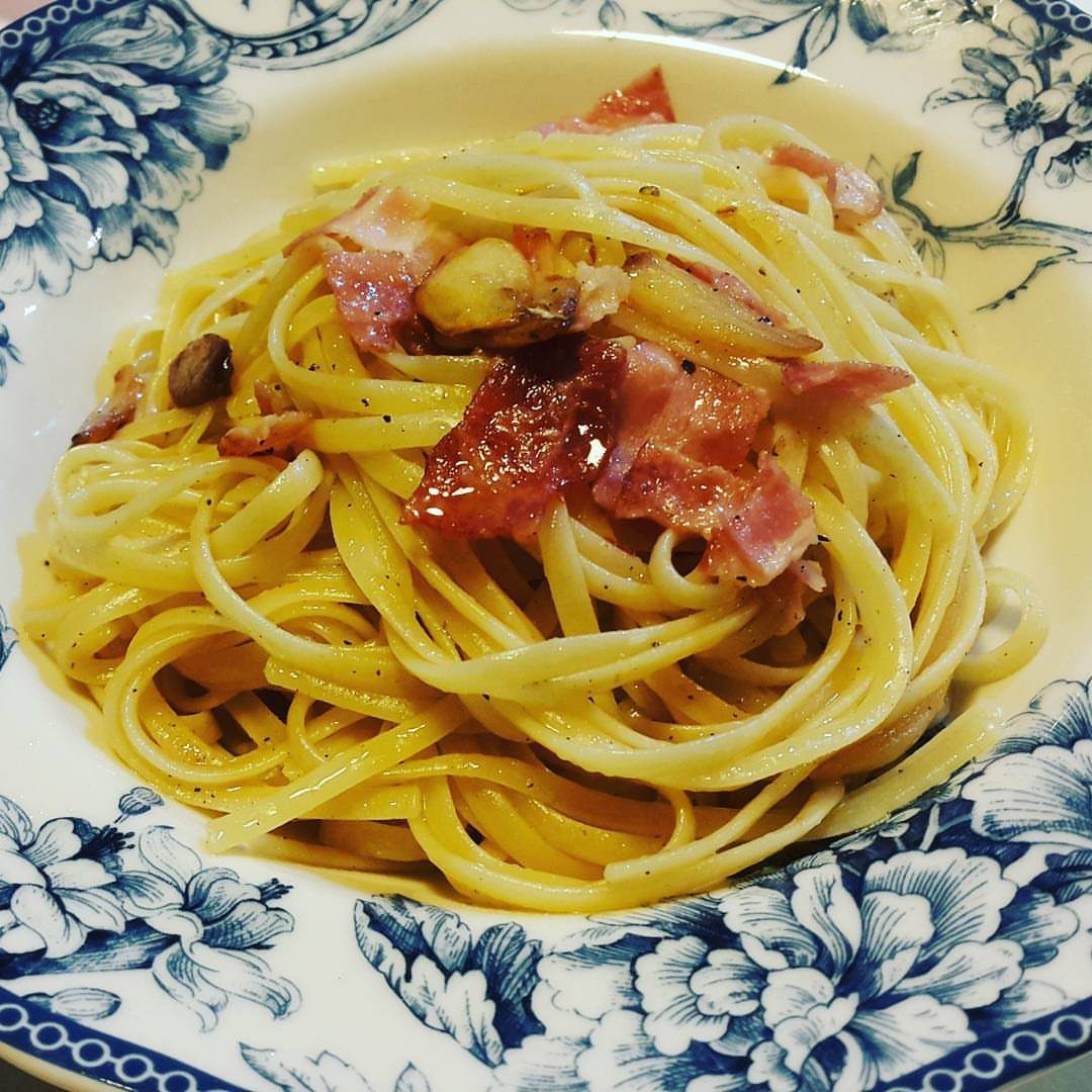Spaghetti pasta mixed with crispy bacon and black pepper served in a white bowl with a blue floral pattern.