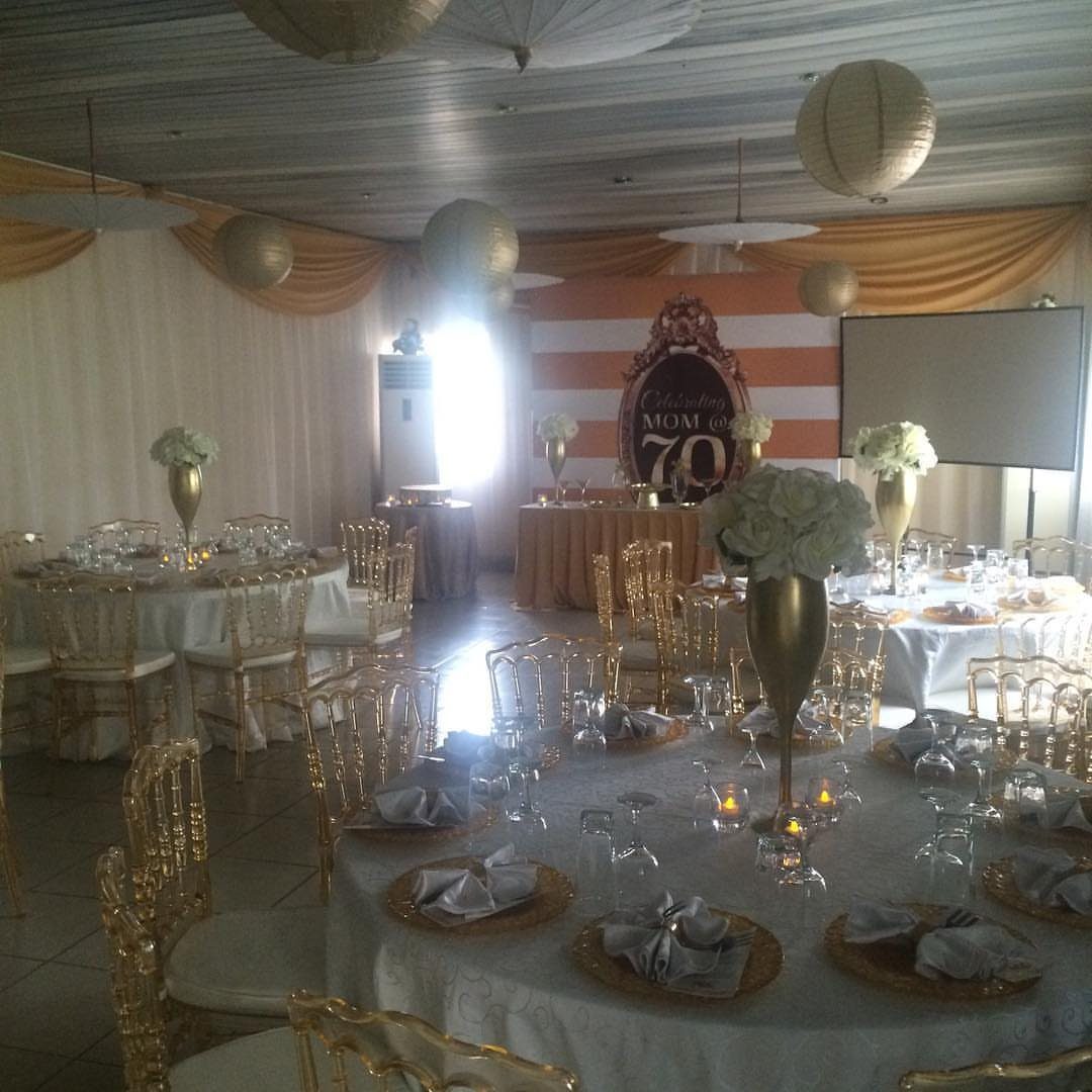 Elegant banquet tables set with white linens, gold chairs, and floral centerpieces in a decorated hall.