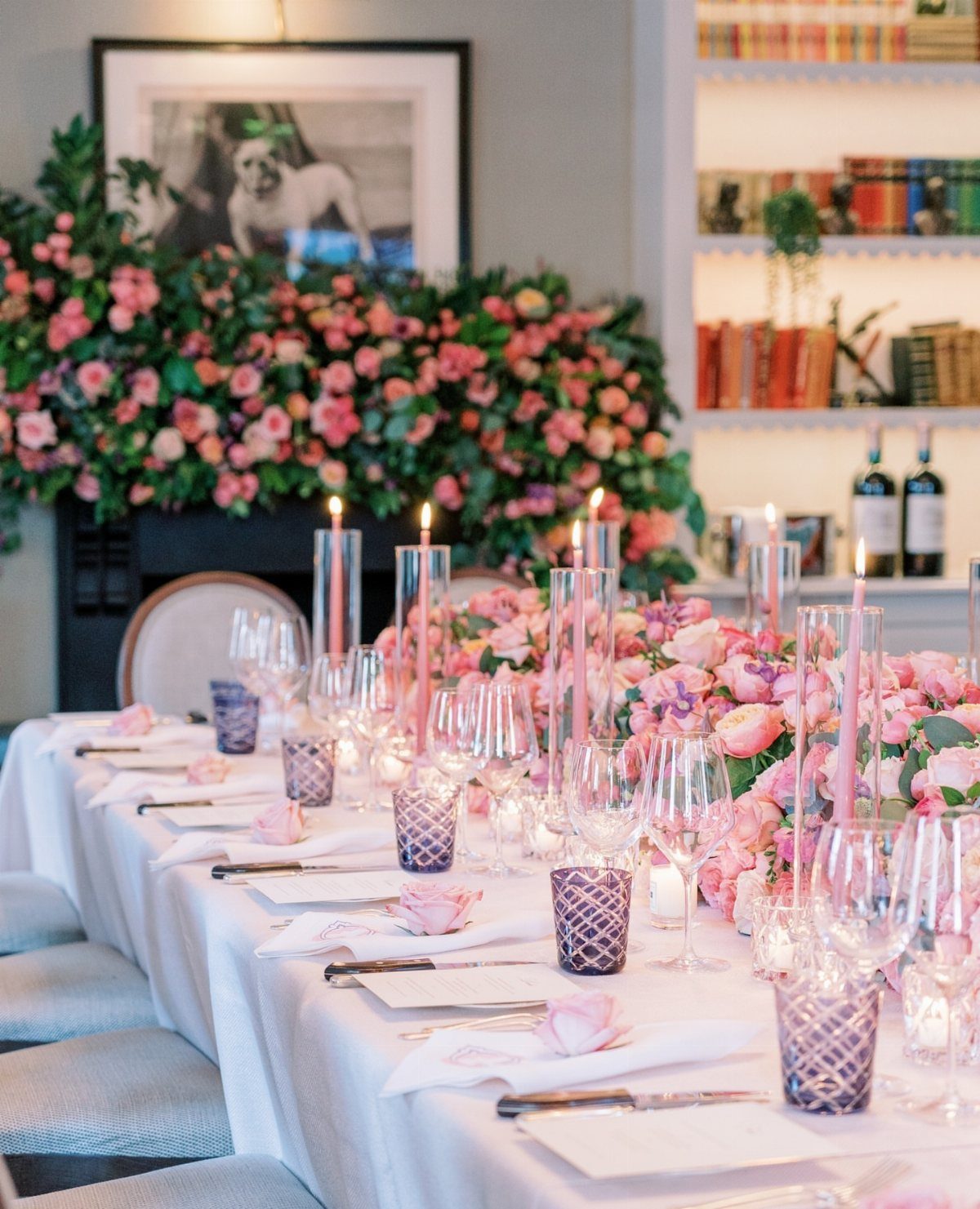 An elegantly set long dining table featuring pink floral centerpieces and tall pink taper candles.