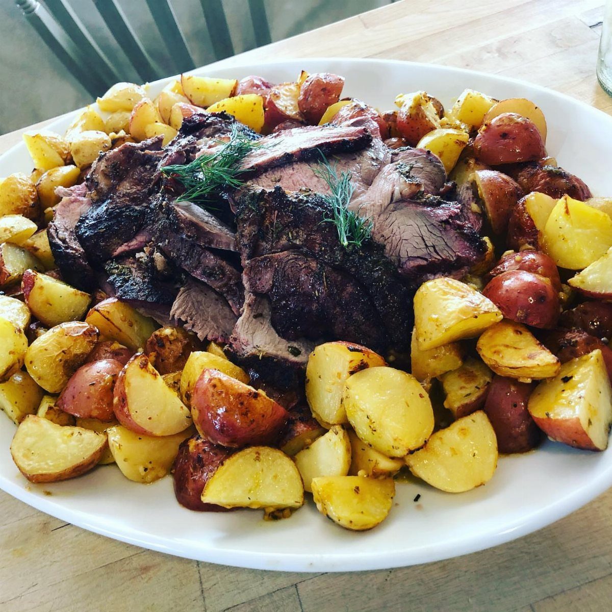 Roasted meat slices surrounded by golden and red roasted potatoes on a white platter.