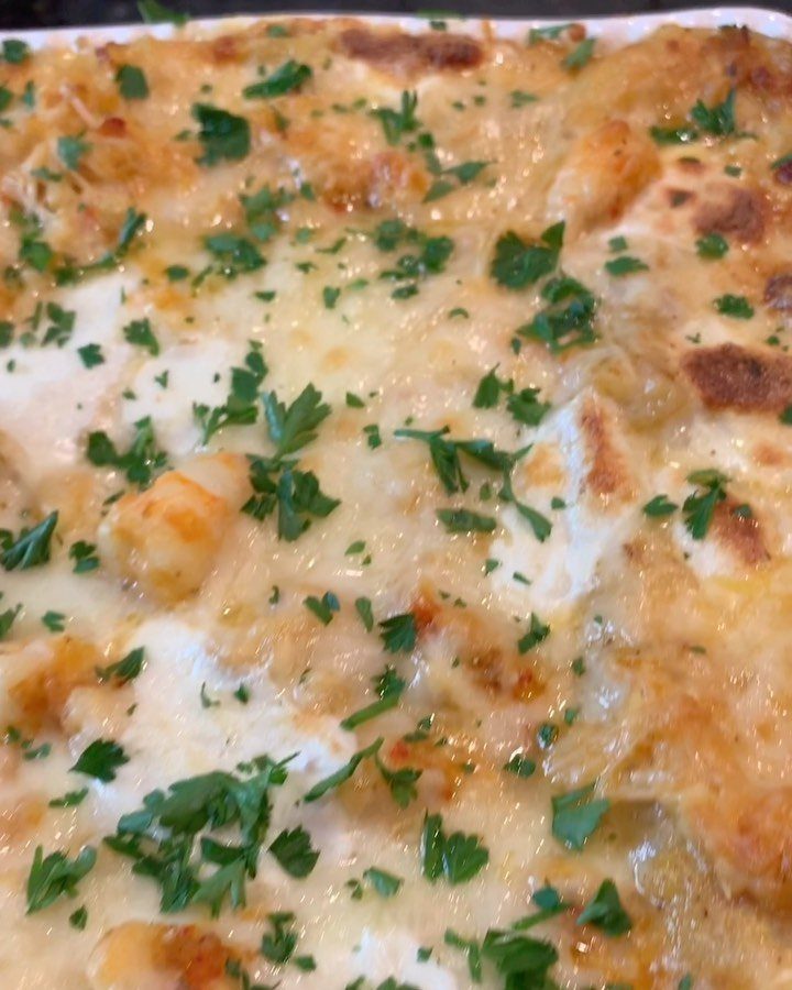 Close-up of baked seafood lasagna with melted golden cheese, creamy white sauce, shrimp, and fresh green parsley garnish.