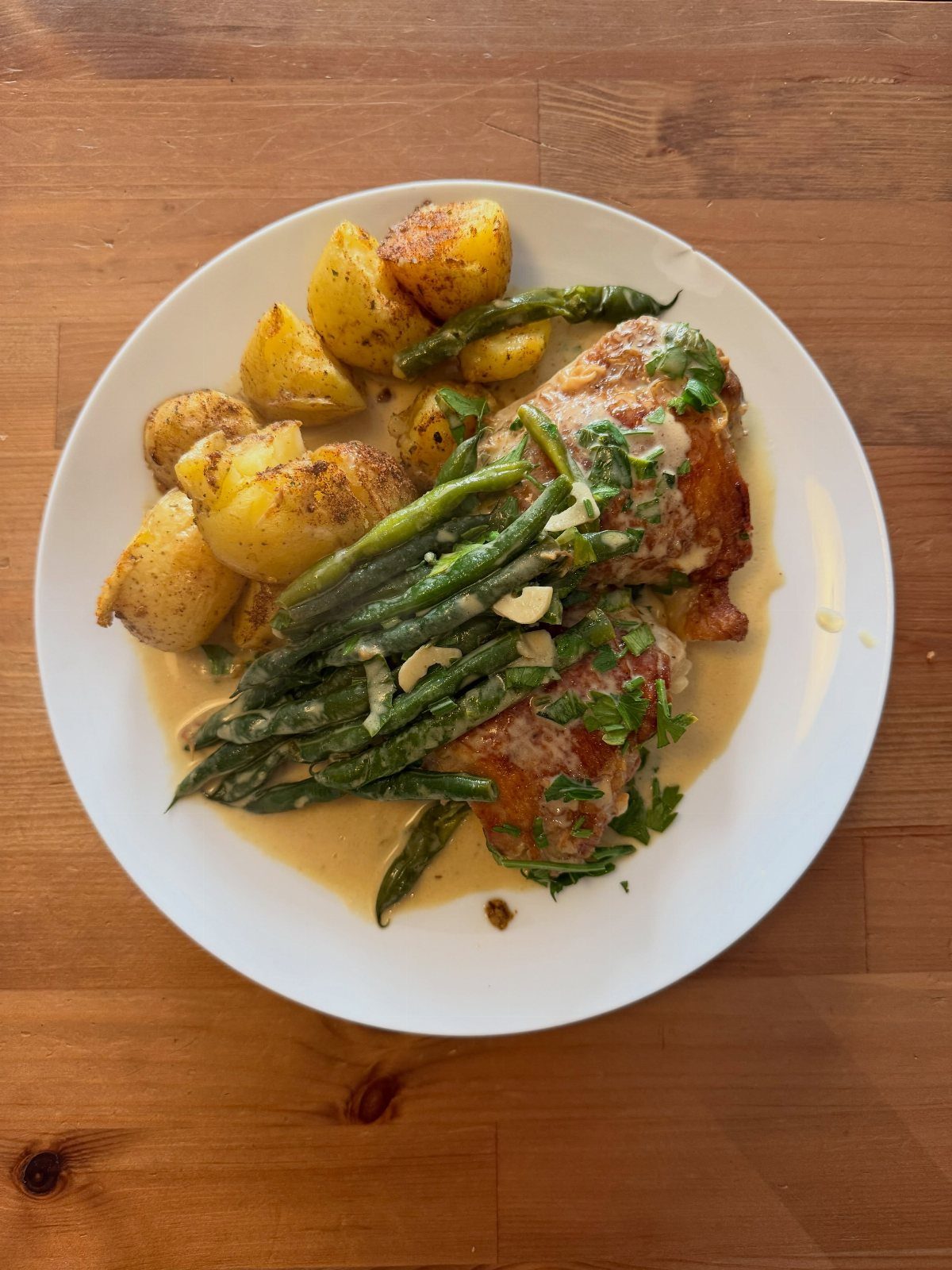 Plate of buttermilk chicken thighs with asparagus and roasted potatoes on a wooden table.