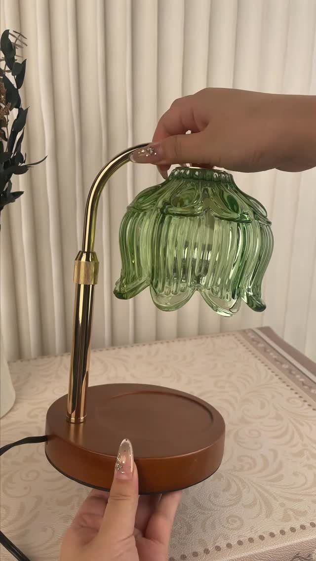 Hands holding a green glass flower-shaped shade over a gold and wood candle warmer lamp.