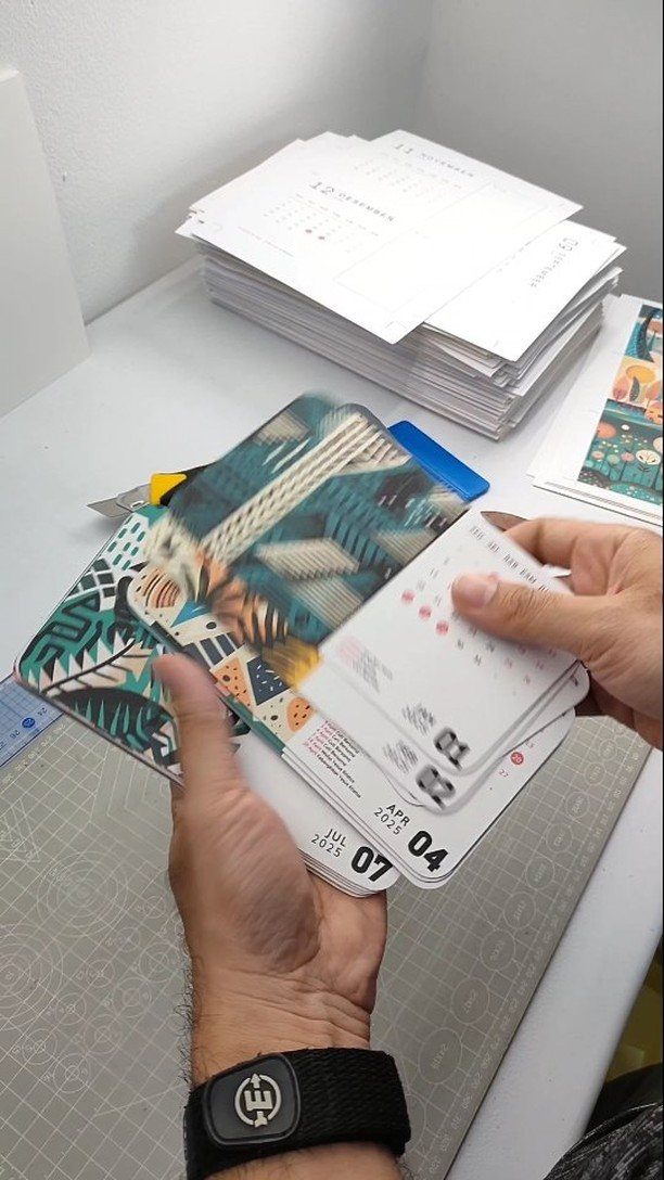 Hands holding a stack of colorful customized calendars with tropical patterns and printed dates.
