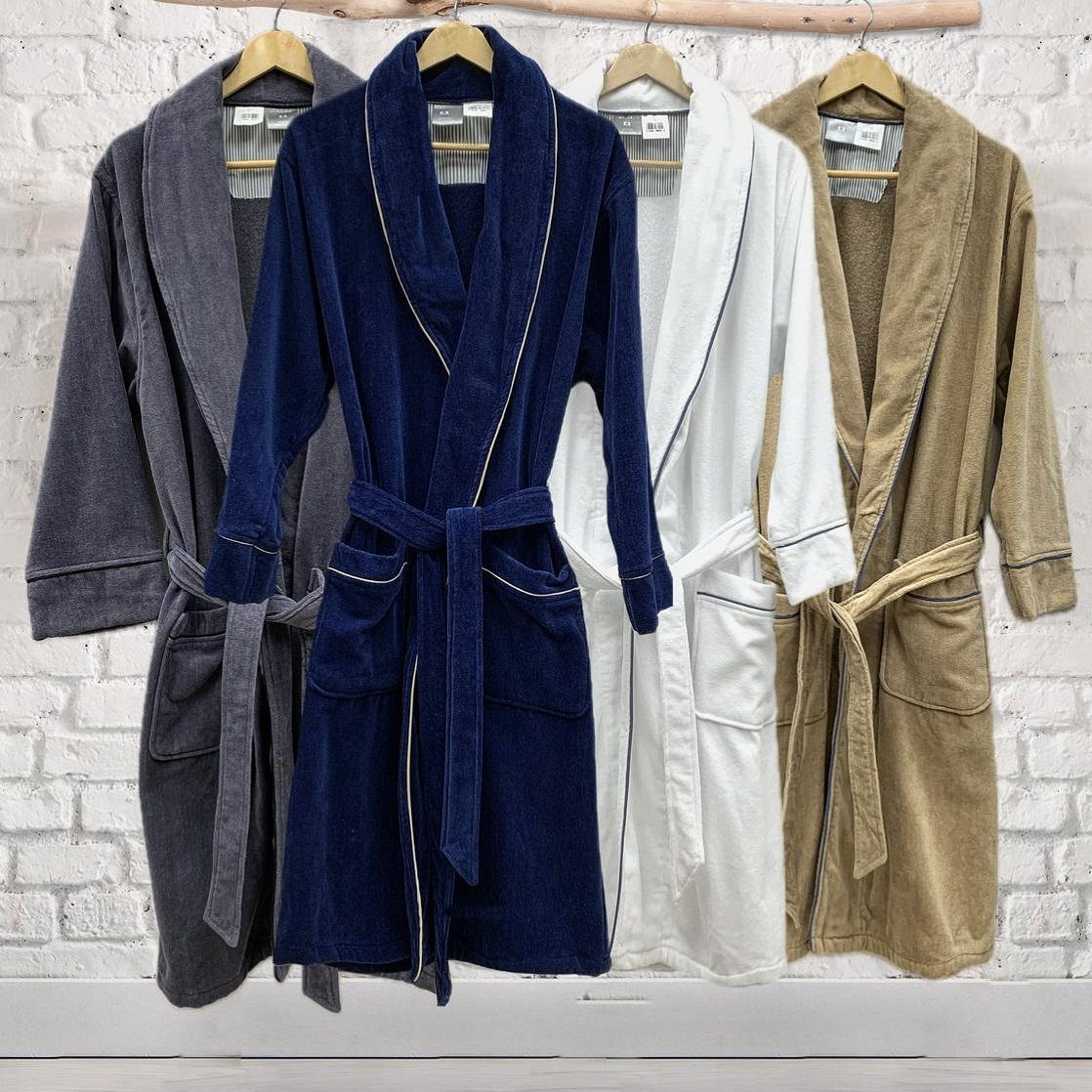 Four plush bathrobes in grey, navy, white, and tan hanging on a wooden rack.