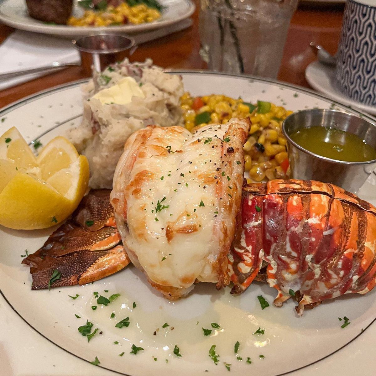 A gourmet lobster tail meal served with mashed potatoes, corn, and lemon wedges.