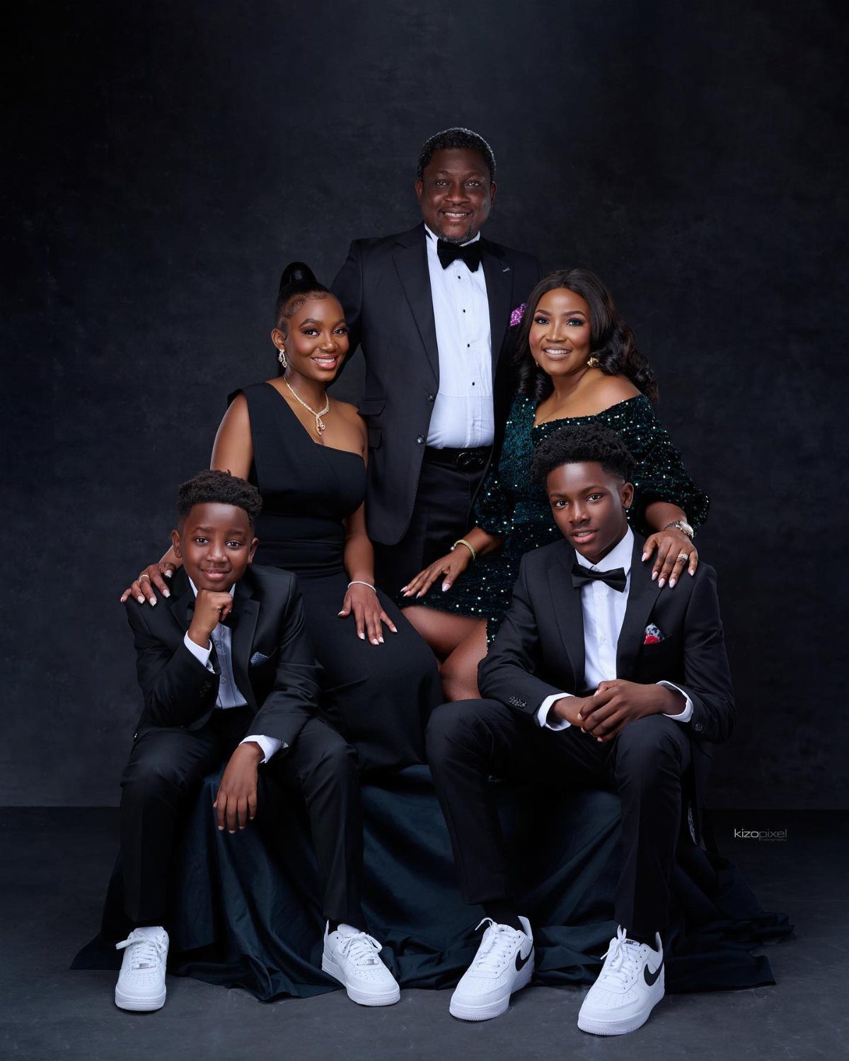 A formal family portrait of six people posing together in elegant black and green attire.