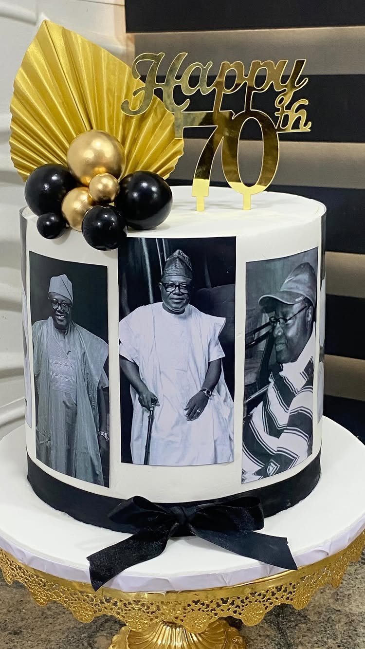 A white birthday cake featuring black and white portraits, gold decorations, and a Happy 70th topper.