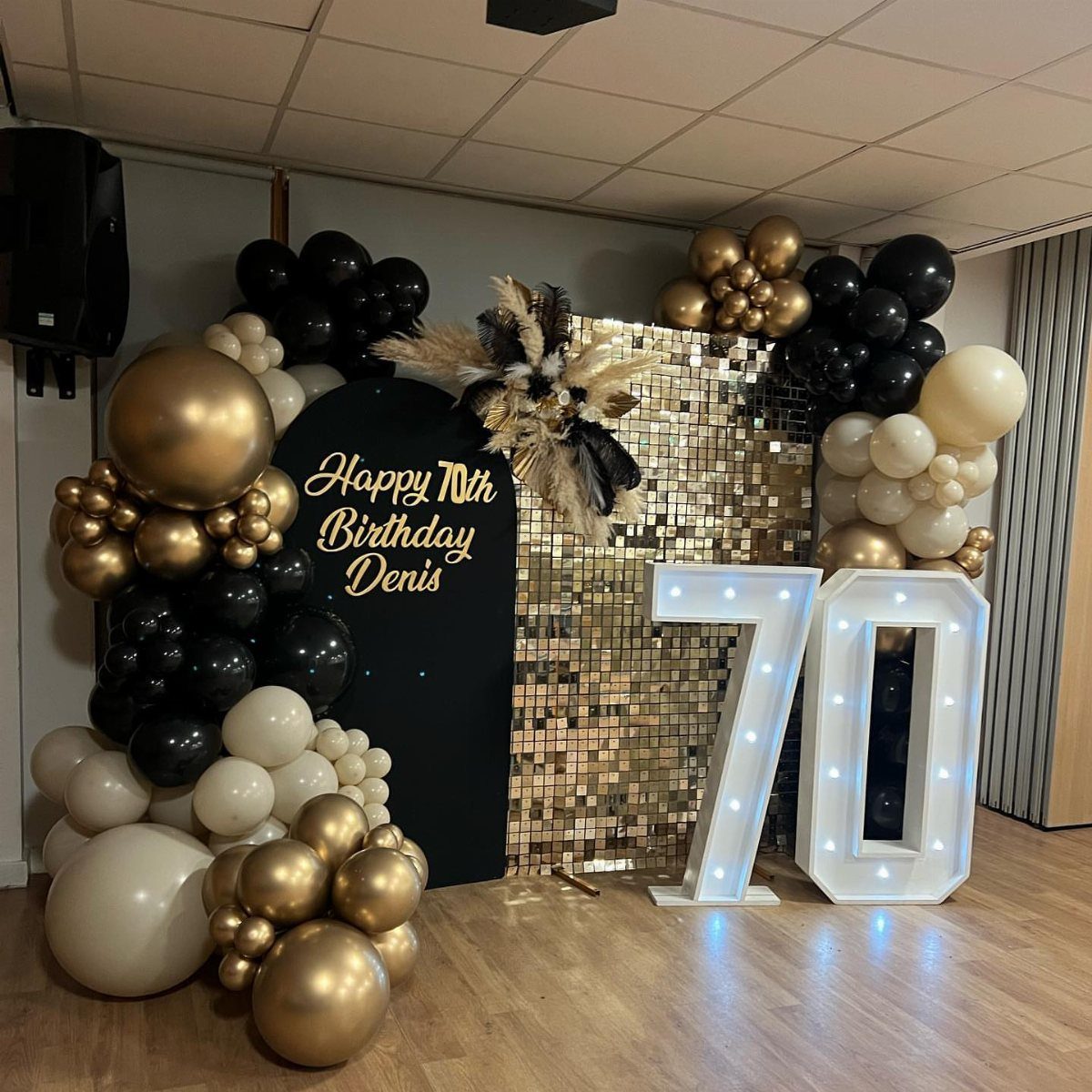 Black and gold balloons surrounding a gold sequin backdrop and a large lit number 70.
