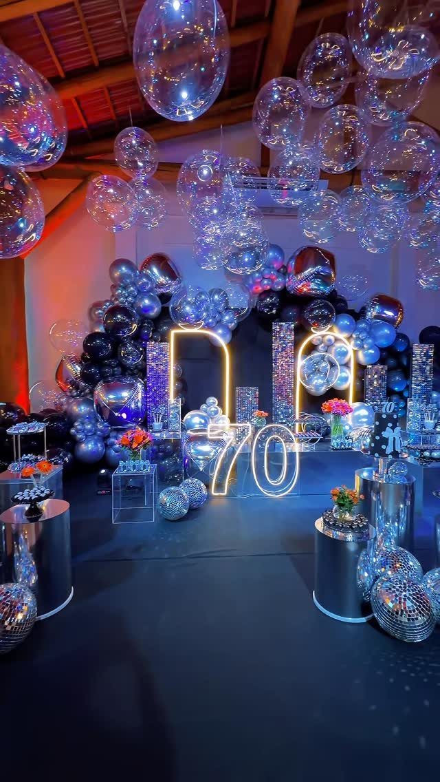 A festive 70th birthday party decoration with glowing neon numbers, blue balloons, and silver disco balls.