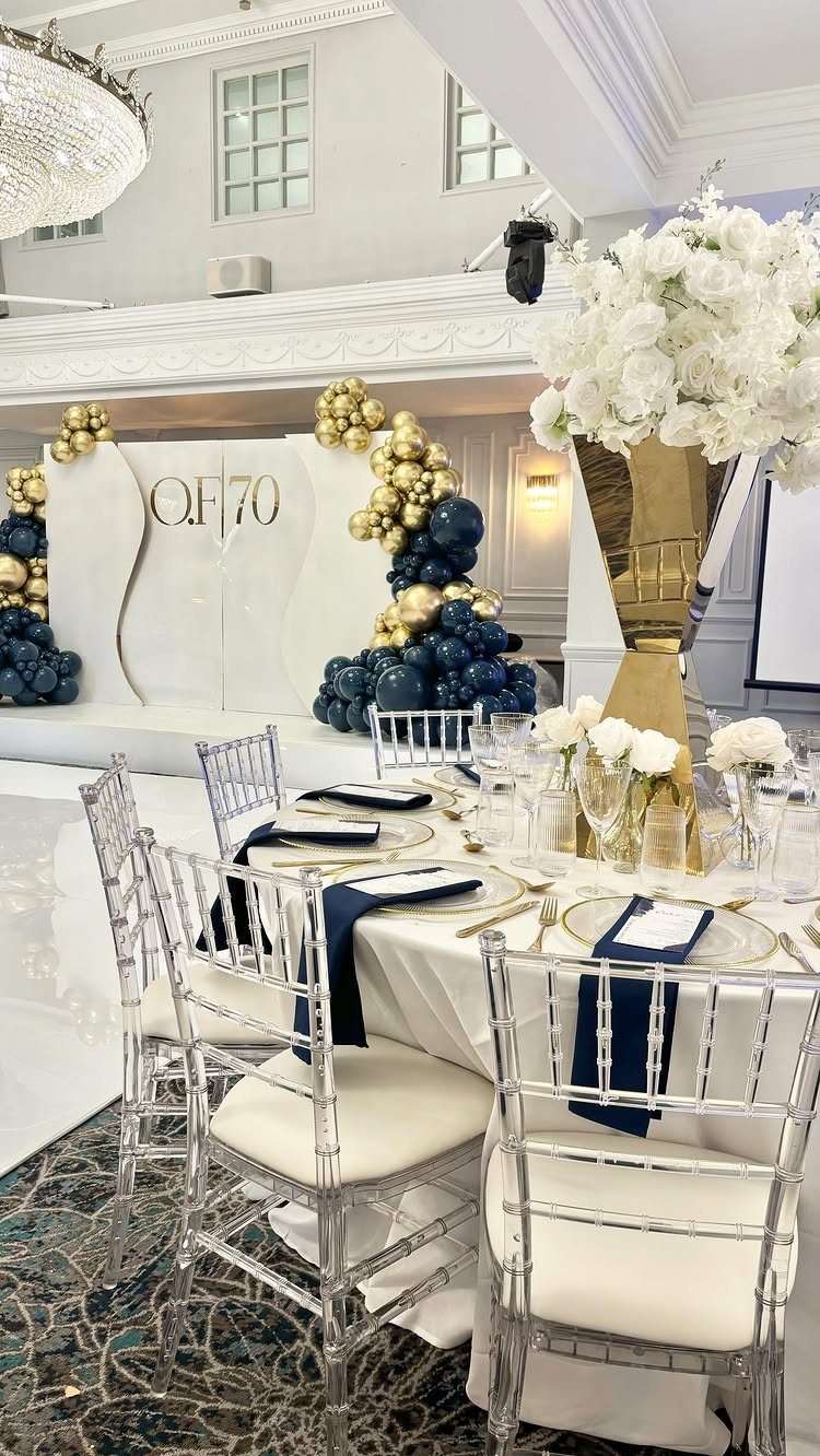 Elegant dining table set with navy napkins and gold cutlery in front of a 70th birthday backdrop.