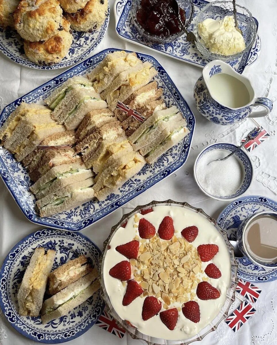High tea spread with sandwiches, scones, and strawberry cake on Union Jack themed blue and white china.