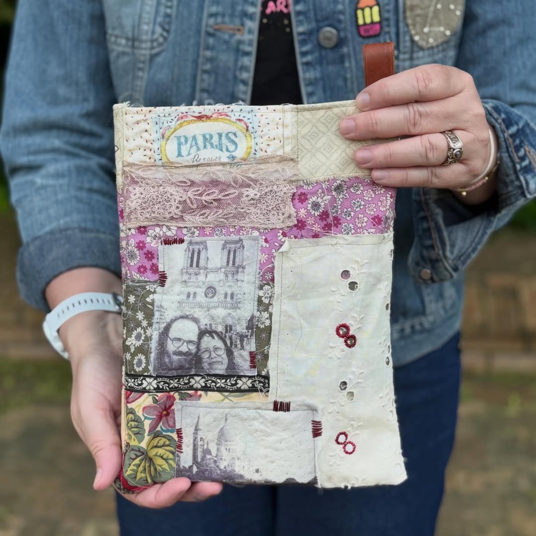 Person holding a handmade fabric travel memory book with Paris-themed patches, lace, and photos.