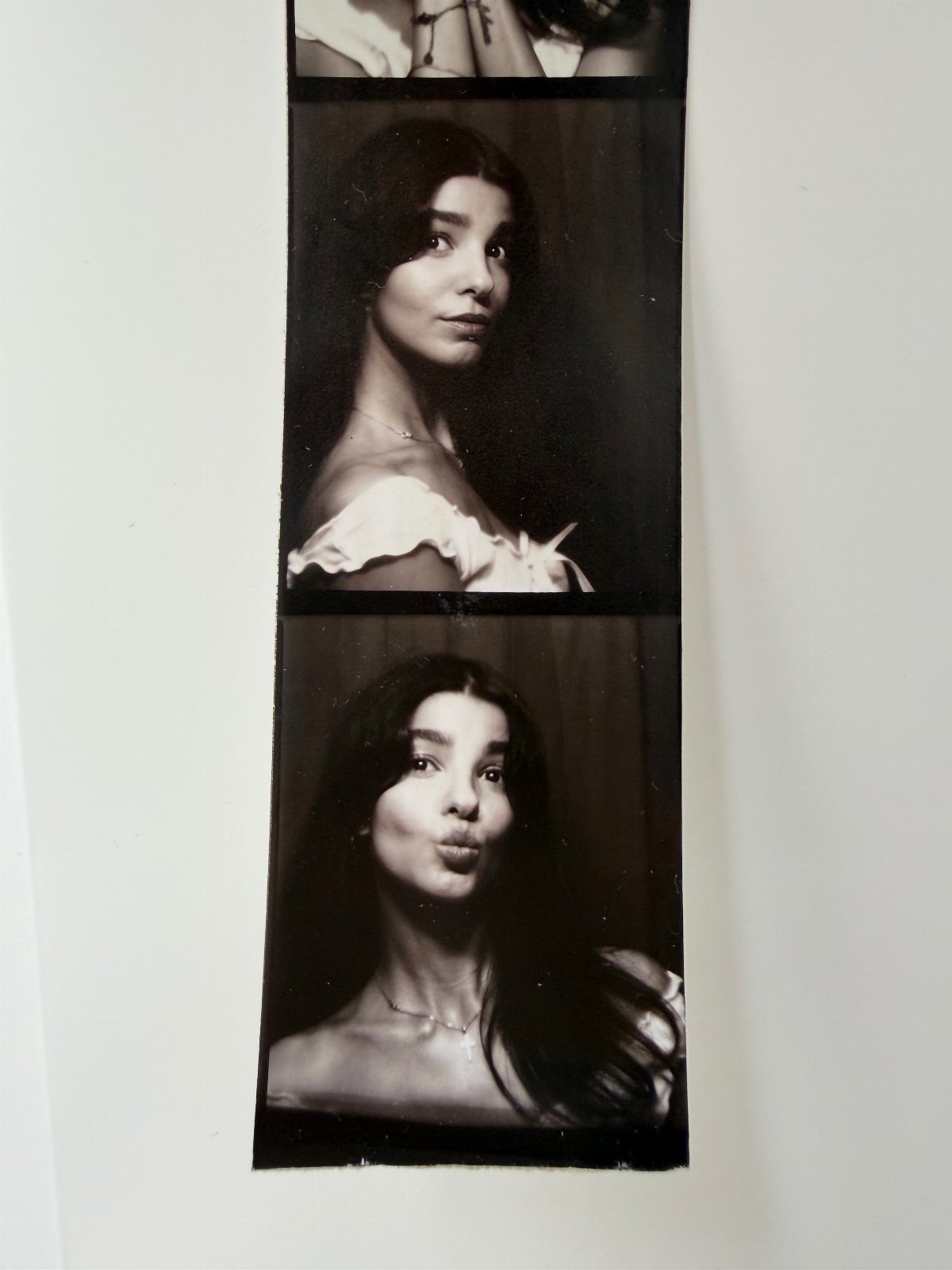 Vertical strip of two black and white instant photos showing a woman posing playfully against a white wall.