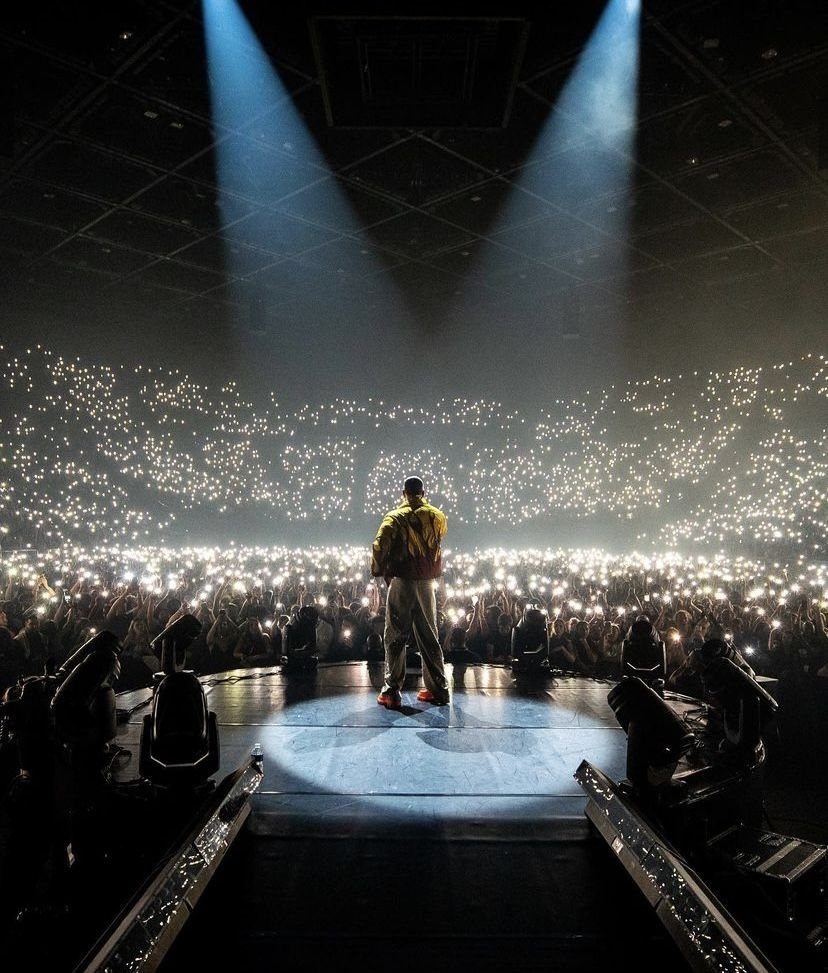A musician performs on a lit stage before a massive crowd holding up glowing phones.