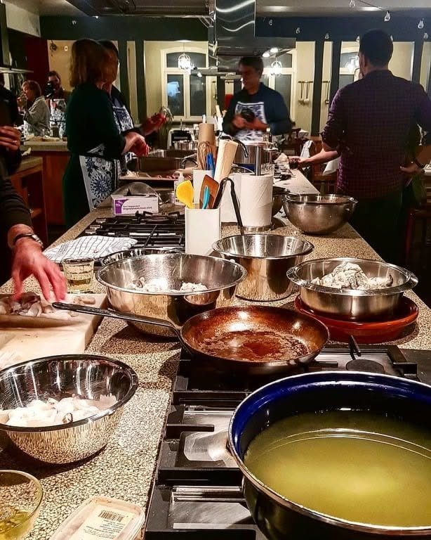 Stainless steel bowls and cooking pots on a kitchen counter with people preparing food.