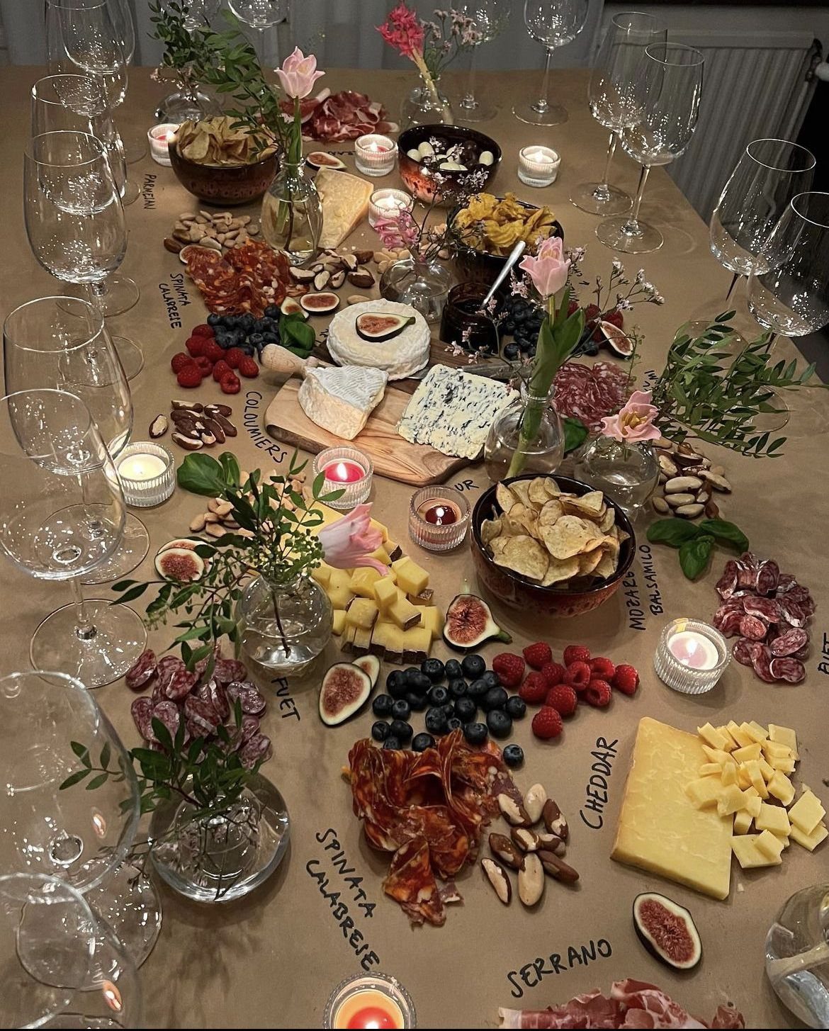 A long table spread with a variety of cheeses, meats, fruits, and flowers for a party.