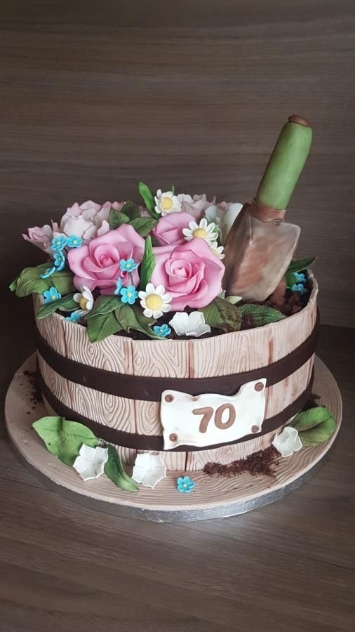 A decorative barrel-shaped cake with pink roses, green leaves, and a small shovel.