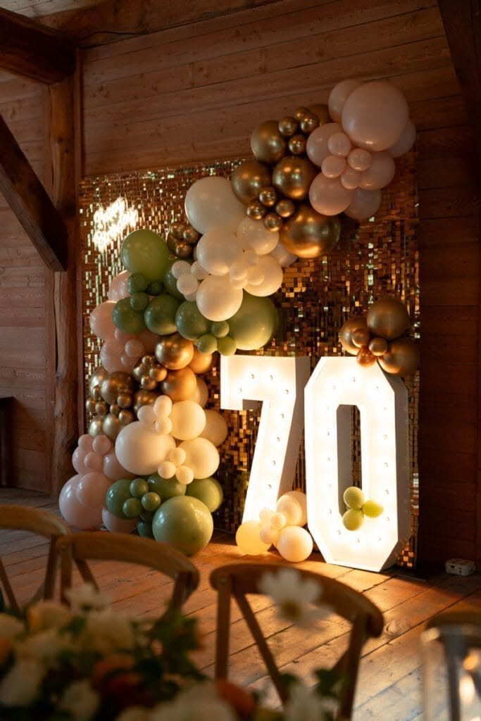 Large glowing marquee numbers 70 set against a gold sequin backdrop and balloon arch.