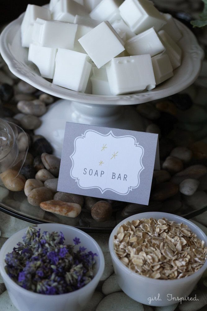 White soap bars in a pedestal dish surrounded by lavender, oats, and smooth stones.