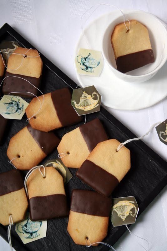 Chocolate-dipped tag-shaped cookies arranged on a black tray and inside a white teacup.