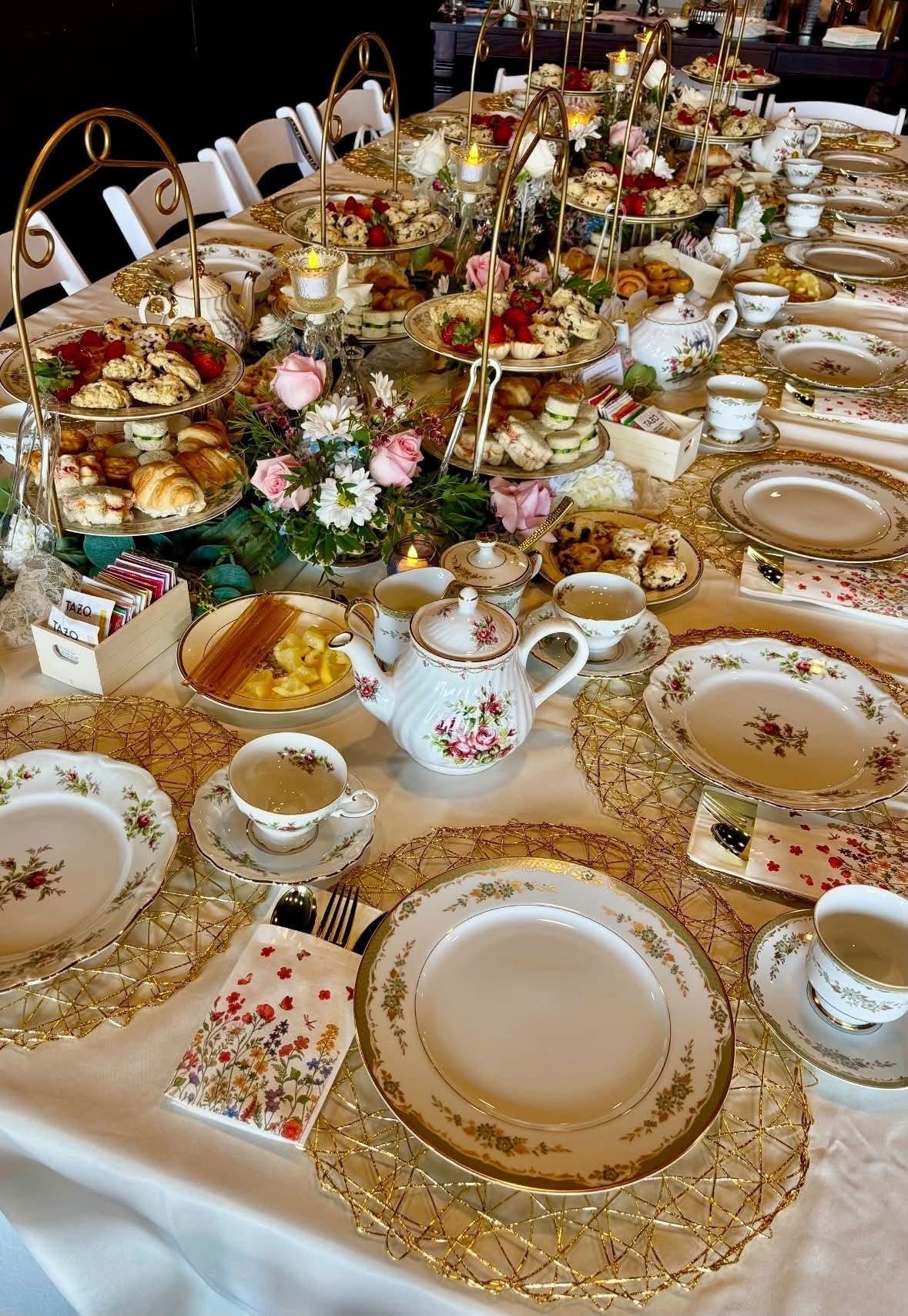 A long table set for afternoon tea with tiered pastry stands, floral arrangements, and fine china.