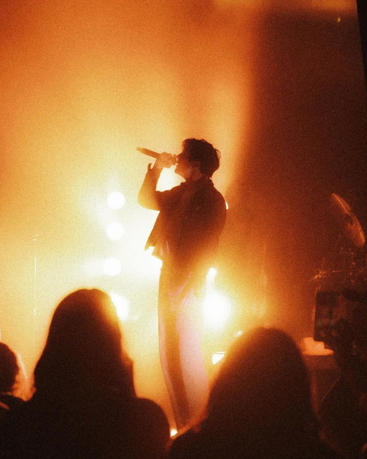 A silhouette of a singer performing on a brightly lit stage with orange light.