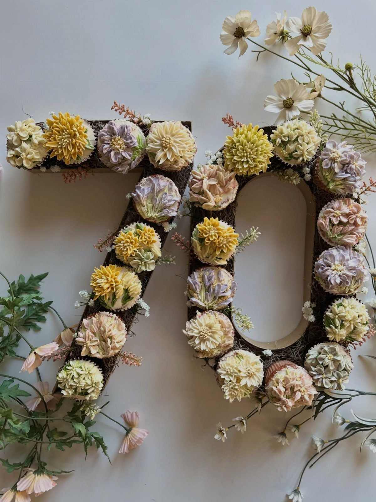 Large number seventy made of cupcakes in pastel colors with white flowers and green leaves.