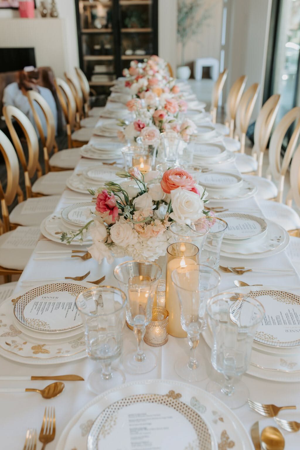 An elegantly set long dining table with floral centerpieces, gold cutlery, and glowing candles.