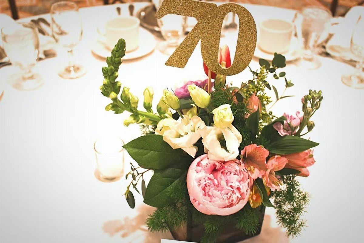 A floral centerpiece with a gold seventy topper on a white table.