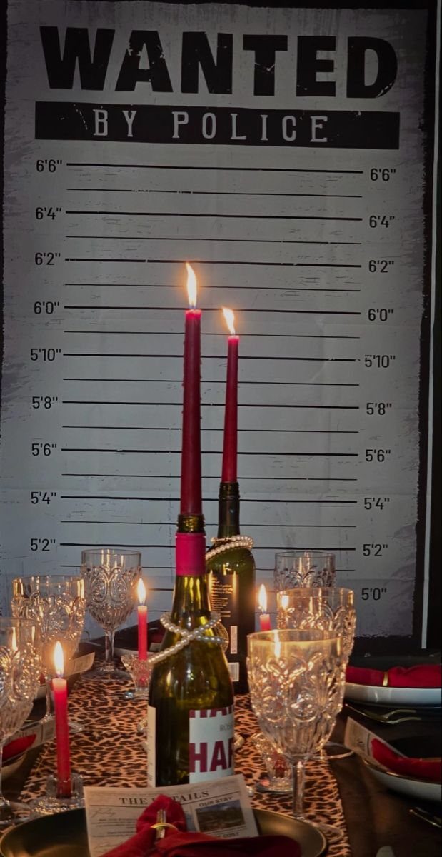 A decorated dinner table with red candles, crystal glassware, and a wanted poster backdrop.