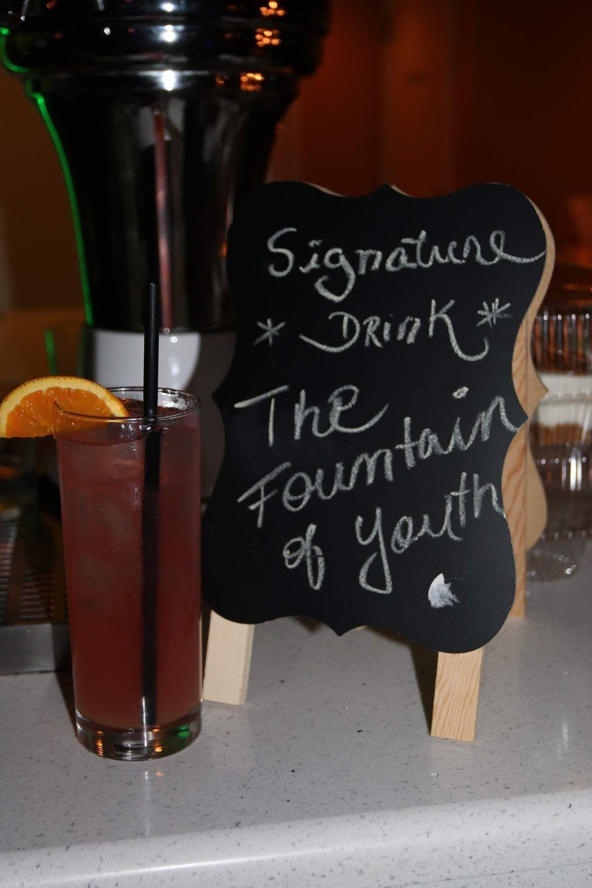 A red cocktail with an orange slice next to a chalkboard sign on an easel.