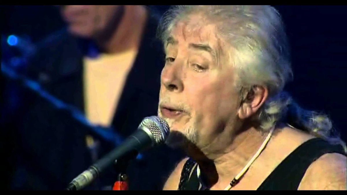 An older woman with grey hair singing passionately into a silver microphone on stage.
