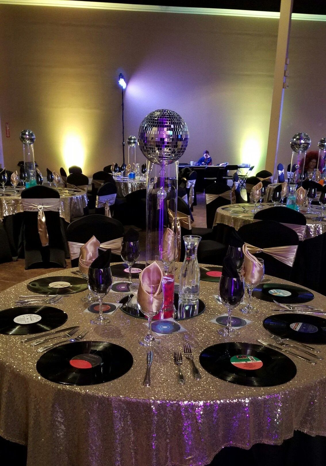 A banquet table set with gold sequins, vinyl record placemats, and a disco ball centerpiece.