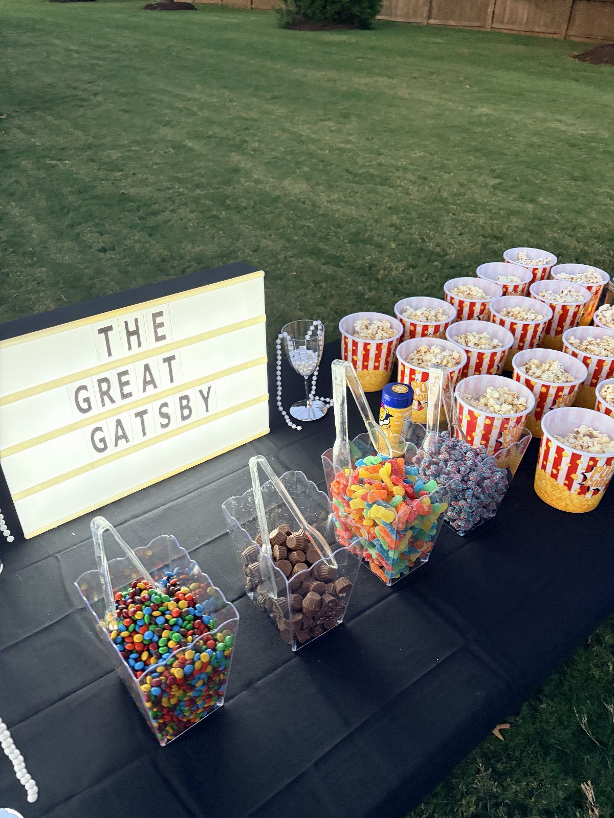 A snack table with popcorn, gummy candies, and chocolates under a Great Gatsby lightbox sign.